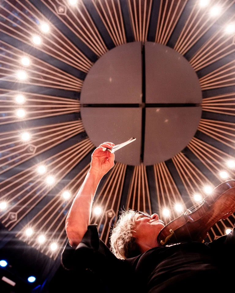 Violinistin in Aktion unter bemerkenswerter Deckenbeleuchtung. Die Perspektive betont das dramatische Lichtspiel im Konzertsaal.