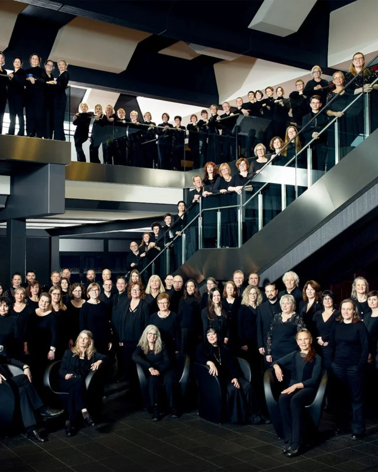A large group of people in black attire pose on a modern, multi-level staircase. Group photo setting with modern architecture.