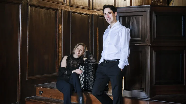 Two people (Marie-Andrée Joerger und Vincent Dubois) pose in a room with large organ pipes and intricate wood carvings, creating a historical and musical atmosphere.
