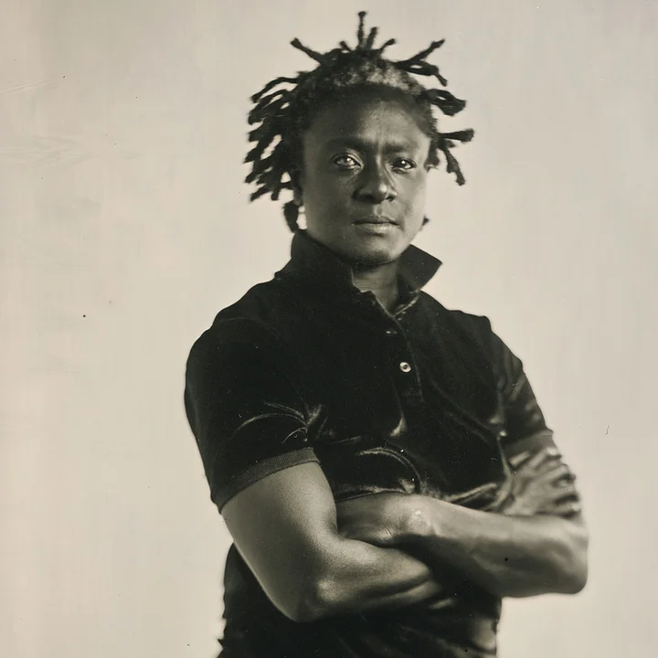 Black-and-white portrait of Bintou Dembélé, looking seriously into the camera with her arms crossed.