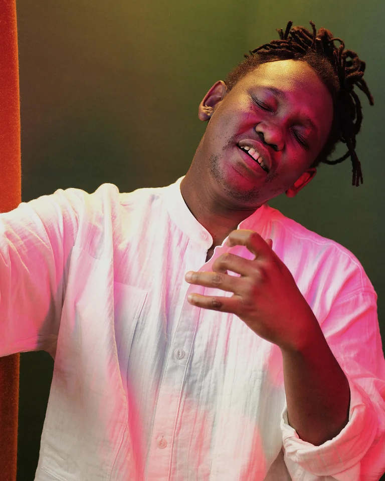 Eine Person (Abel Selaocoe) mit geschlossenen Augen und einem entspannten Lächeln trägt ein weißes Hemd und scheint Musik zu genießen.