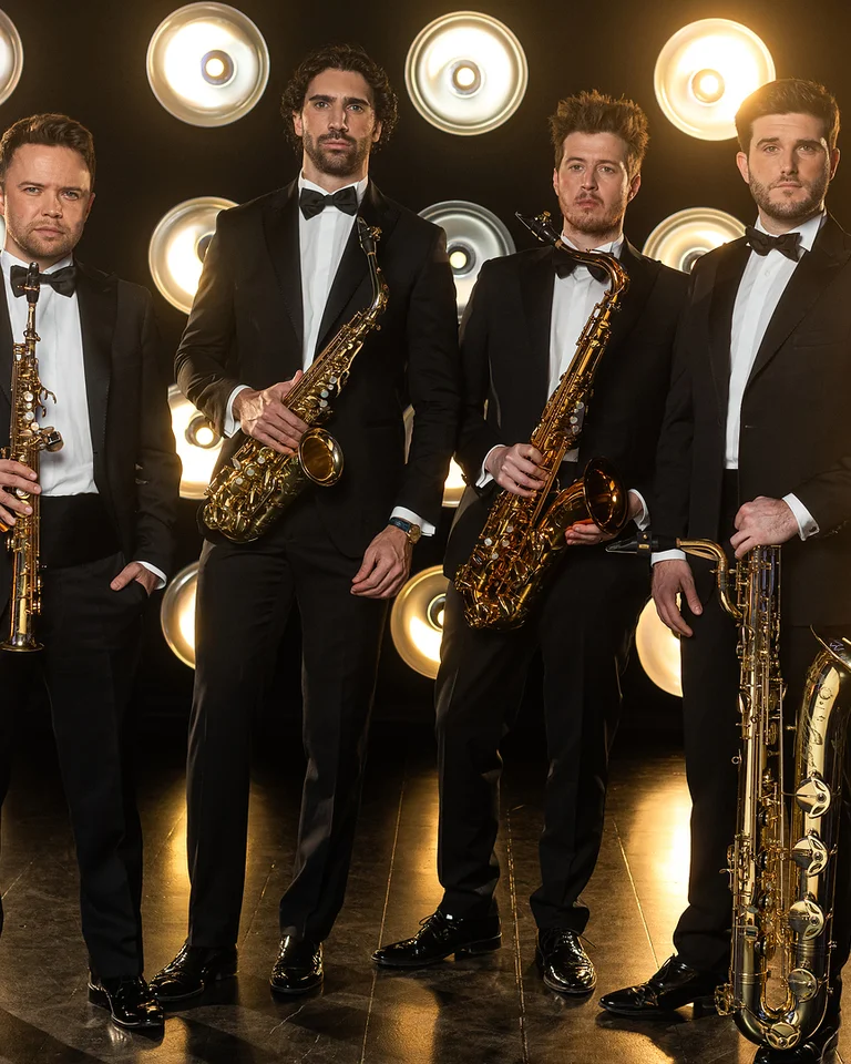 Vier Männer (SIGNUM Quartett) in Smokings stehen mit Saxophonen vor einer leuchtenden Hintergrundwand, die mit runden Lichtern dekoriert ist.