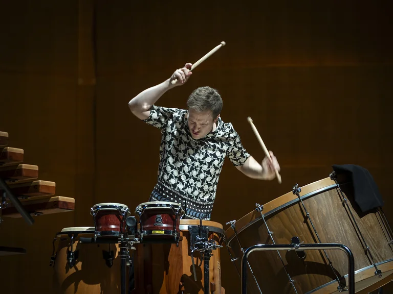 Ein Musiker (Christoph Sietzen) spielt leidenschaftlich Schlaginstrumente auf der Bühne, umgeben von verschiedenen Trommeln. Seine Energie füllt den Raum.
