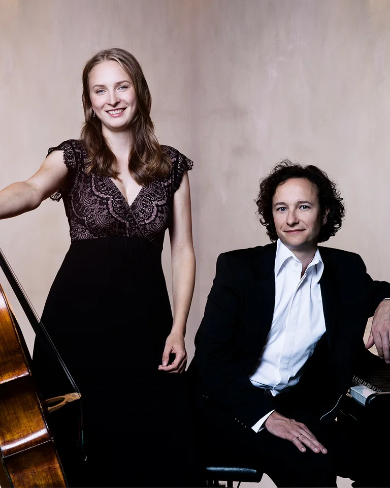 Eine Frau steht mit einem Cello neben einem sitzenden Mann am Flügel. Beide tragen elegante Abendkleidung.