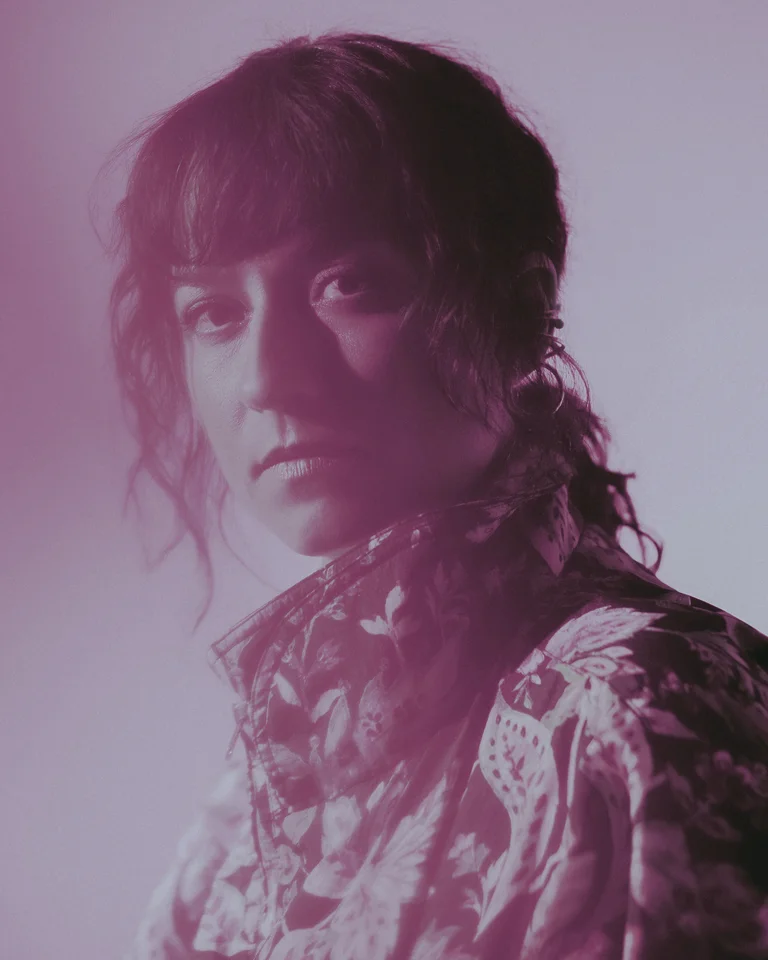 Lucia Cadotsch looks earnestly into the camera, in a softly lit, rose-tinted room. Her expression is contemplative.