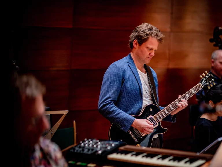 Ensemble Resonanz: Ein Musiker spielt E-Gitarre während einer Probe. Im Hintergrund sind andere Musiker mit verschiedenen Instrumenten zu sehen.