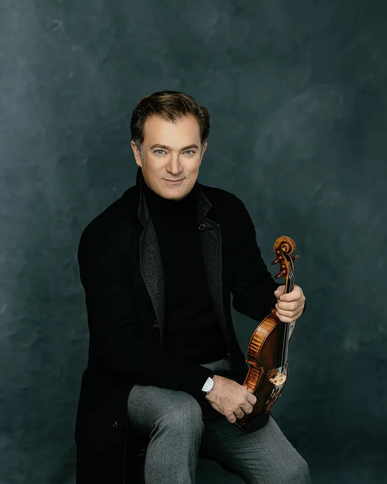 Ein Bild von Renaud Capuçon: Ein Mann in dunkler Kleidung sitzt und hält eine Geige. Der Hintergrund ist neutral und schlicht gestaltet.
