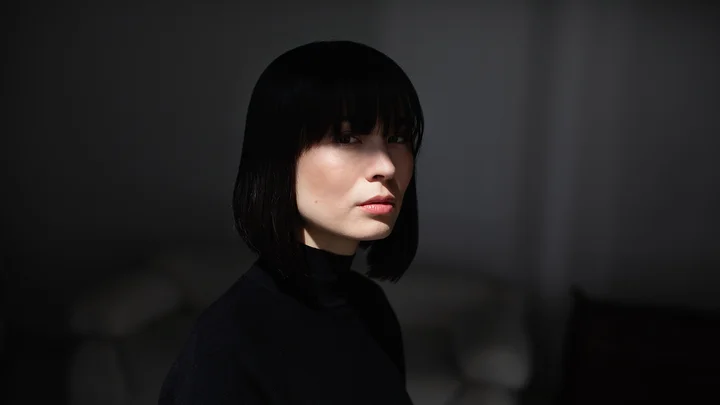 Eine Frau (Alice Sara Ott) mit schwarzen Haaren und Pony blickt ernst in einem dunklen Raum. Der Hintergrund ist verschwommen.