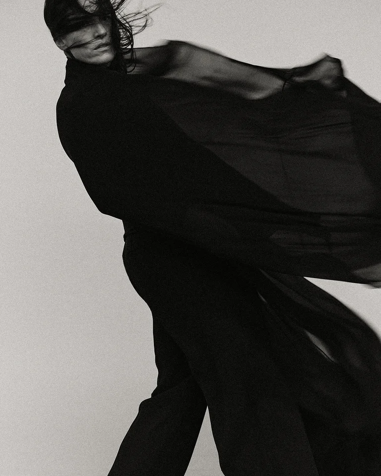 A person (Carminho) in black clothing moves dynamically, with flowing fabric, reminiscent of modern expressive dance.