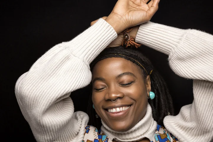 Malika Tirolien crosses her arms above her head and smiles with her eyes closed.