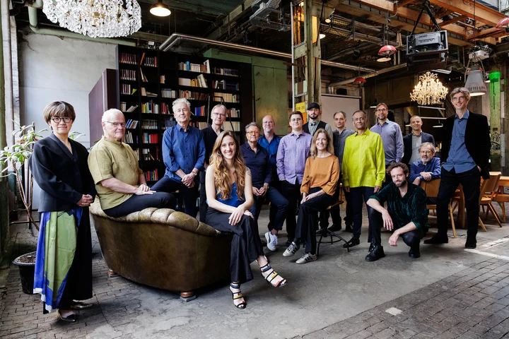 Die Mitglieder des Ensemble Modern stehen beziehungsweise sitzen in einem Raum mit künstlerischem Interieur, Büchern und Vintage-Dekorationen im Hintergrund.