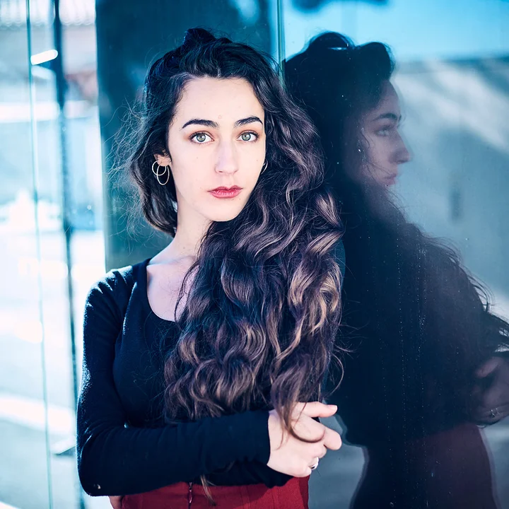 Amandine Sanchez, leaning against a reflective glass surface and looking into the camera.