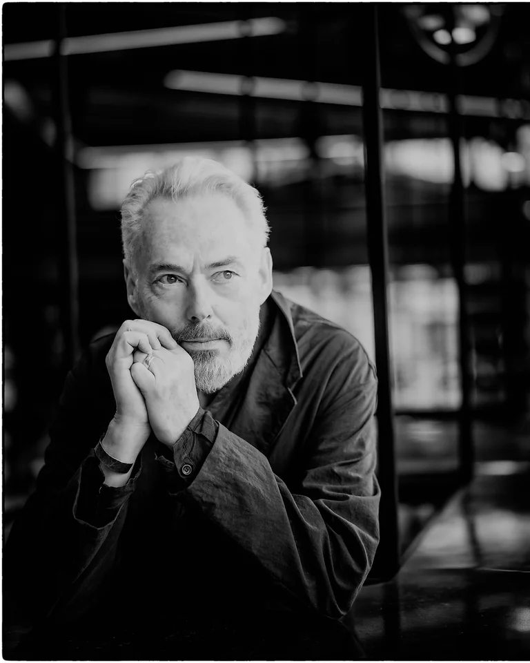 Black and white photo of a contemplative man (Mark Padmore) in a suit. He's leaning on a railing, gazing sideways.