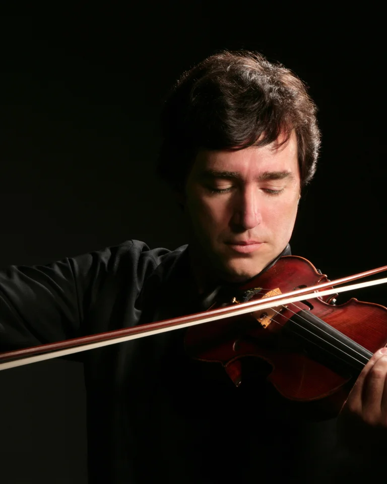 Ein Violinist spielt konzentriert auf einer Geige. Der Hintergrund ist dunkel, wodurch der Fokus auf den Musiker verstärkt wird.