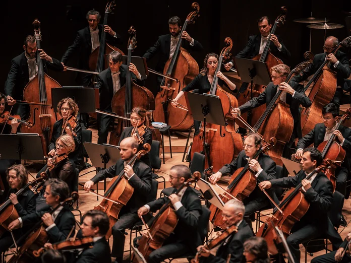 Symphonieorchester (Gewandhausorchester Leipzig) bei einem Konzert. Die Musiker sind mit Geigen, Celli und anderen Streichinstrumenten auf einer Bühne versammelt.