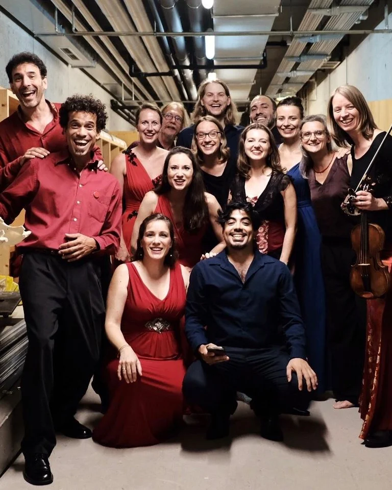 Eine Gruppe von Musikerinnen und Musikern in eleganter Kleidung posiert lächelnd in einem Korridor mit Geigen und Noten.