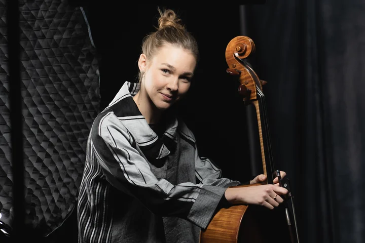 Valerie Fritz hält im abgedunkelten Fotostudio ihr Cello und lächelt.