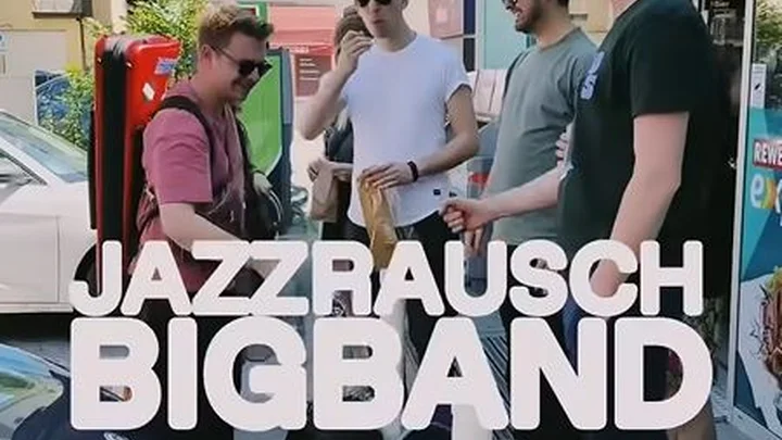 Eine Gruppe von fünf Mitgliedern der Jazzrausch Bigband, die entspannt auf der Straße stehen. Der Schriftzug "Jazzrausch Bigband" ist über das Standbild gelegt.