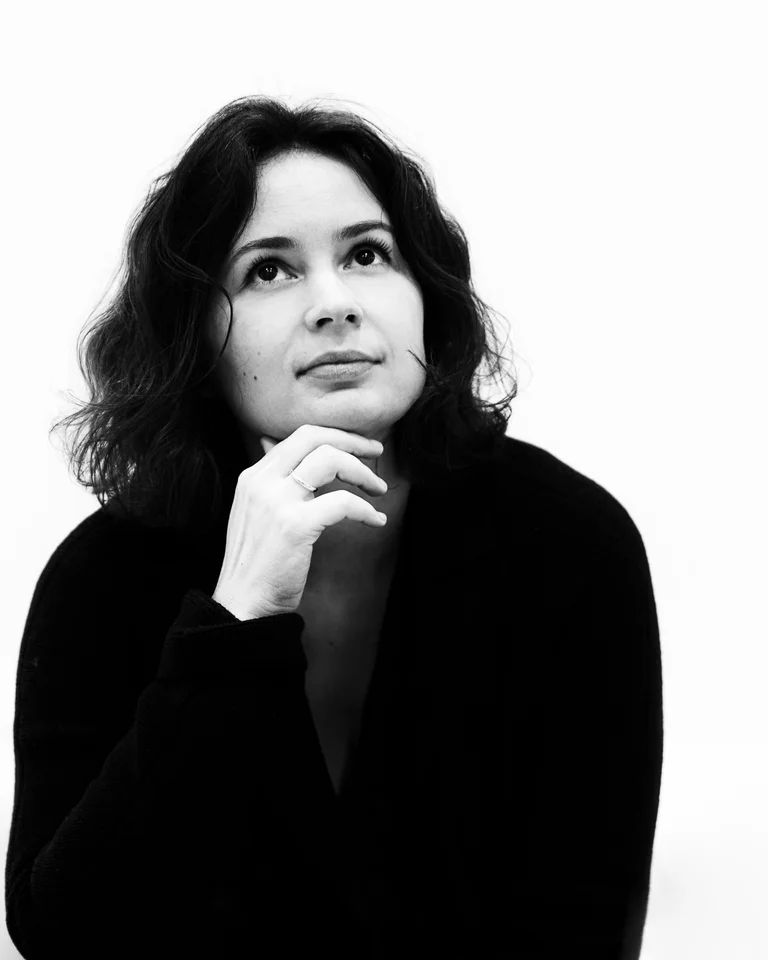 Eine Frau mit lockigem Haar in Schwarz-Weiß. Sie schaut nachdenklich zur Seite und trägt einen schwarzen Pullover.