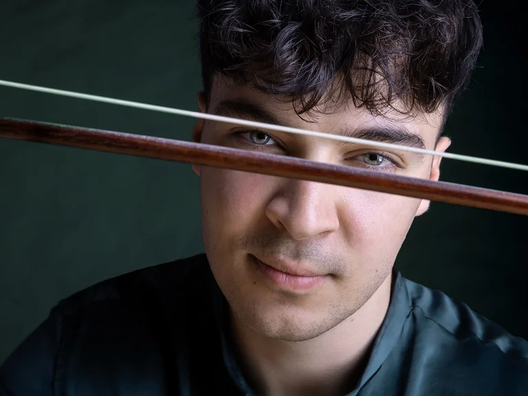 Ein Mann (Petar Pejčić) schaut ernst, während ein Geigenbogen künstlerisch vor seinen Augen platziert ist. Der Hintergrund ist dunkel.