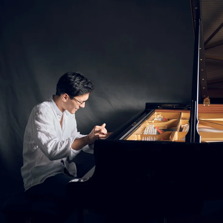 Nuron Mukumi: Ein Mann spielt konzentriert auf einem Flügel in einem abgedunkelten Raum, beleuchtet durch sanftes Licht.