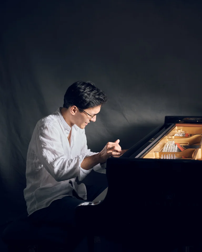 Nuron Mukumi: Ein Mann spielt konzentriert auf einem Flügel in einem abgedunkelten Raum, beleuchtet durch sanftes Licht.