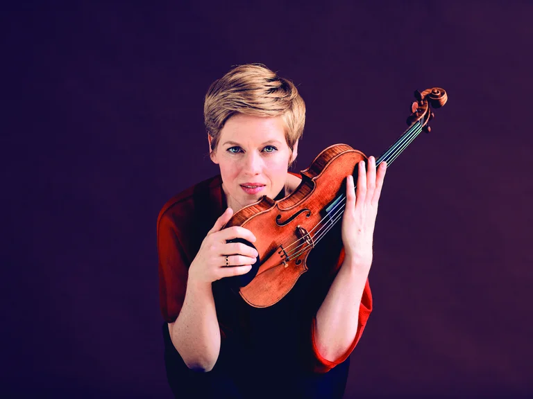 Eine Person (Isabelle Faust) mit kurz geschnittenem Haar hält eine Geige vor einem lila Hintergrund. Sie scheint konzentriert und engagiert zu sein.