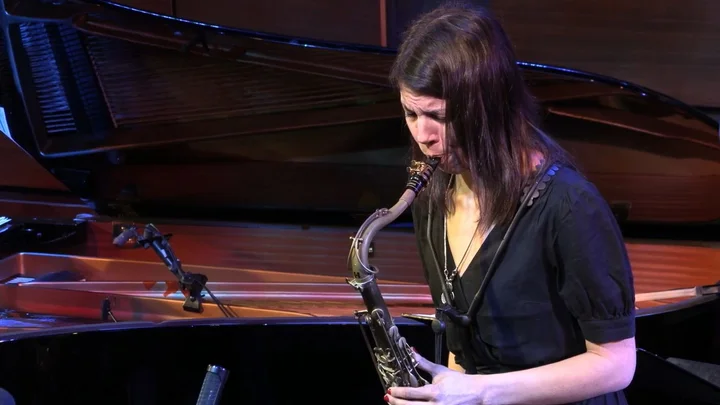 Melissa Aldana spielt Saxophon vor einem Flügel.