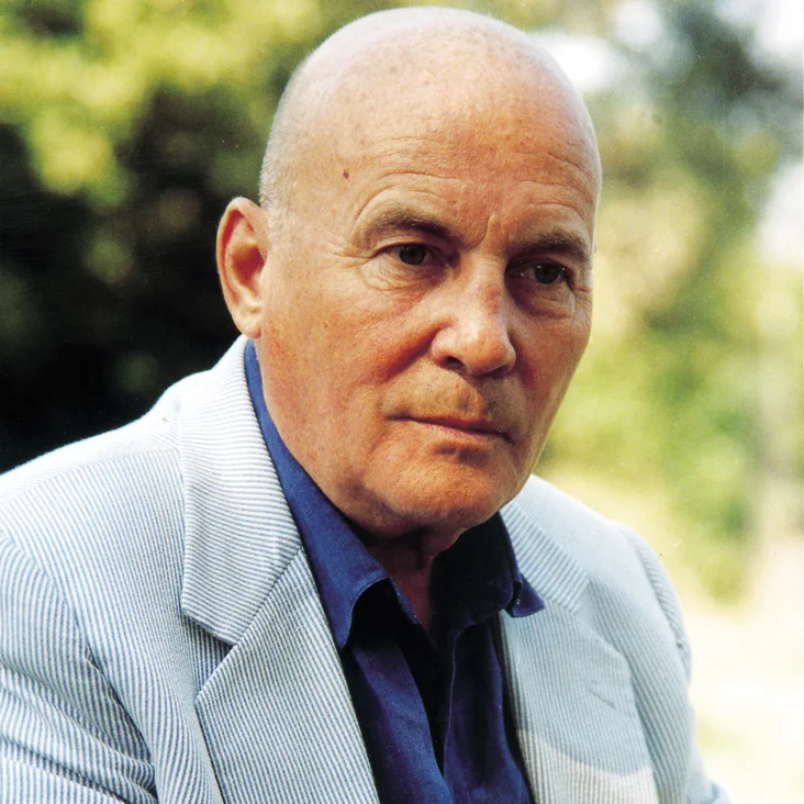 An older man (Hans Werner Henze) in a blue shirt and striped jacket sitting outdoors.