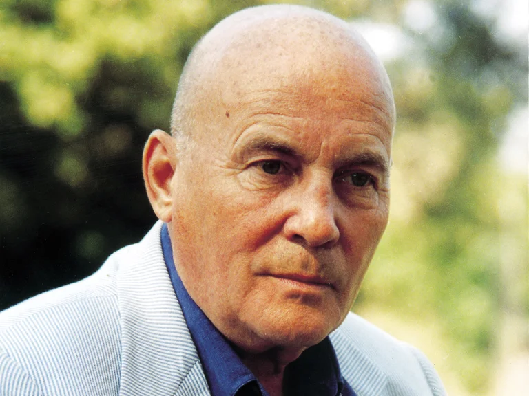 Ein älterer Mann (Hans Werner Henze) in einem blauen Hemd und einem gestreiften Sakko sitzt im Freien.