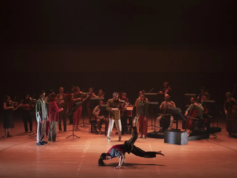 Eine Gruppe von Musikern und Tänzern auf der Bühne, darunter ein Breakdancer in Aktion, mit stimmungsvoller Beleuchtung.