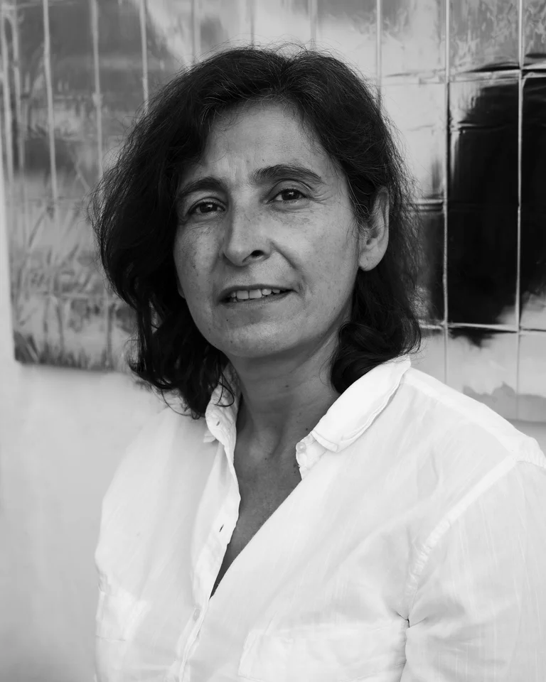 Schwarzweiß-Foto einer Person mit mittellangem Haar, die ein weißes Hemd trägt. Der Hintergrund zeigt eine strukturierte Wand.