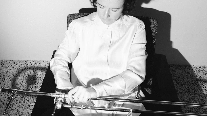 Eine Person in einem weißen Hemd sitzt und hält eine Posaune. Die Fotoaufnahme erfolgt in Schwarzweiß.