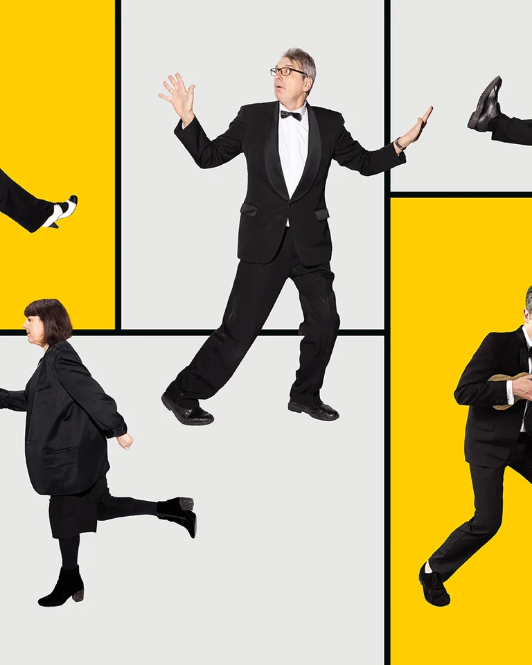 Mehrere Menschen in eleganter Kleidung posieren humorvoll vor einem gelben und grauen Hintergrund. Einige halten Gitarren.