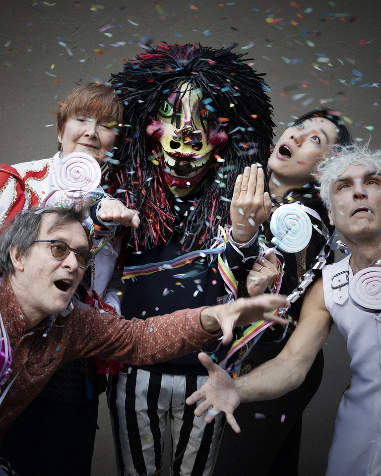 Eine Gruppe von Menschen feiert, während sie Kostüme tragen. Konfetti fliegt in der Luft um sie herum.