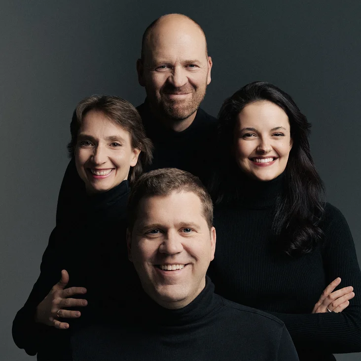 Two men and two women (Cuarteto Casals) in dark clothing smile together against a gray background.
