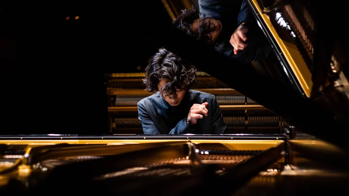 Ein Pianist in dunkler Kleidung spielt konzentriert auf einem Flügel. Die Szene wird dramatisch beleuchtet, was Spannung erzeugt.