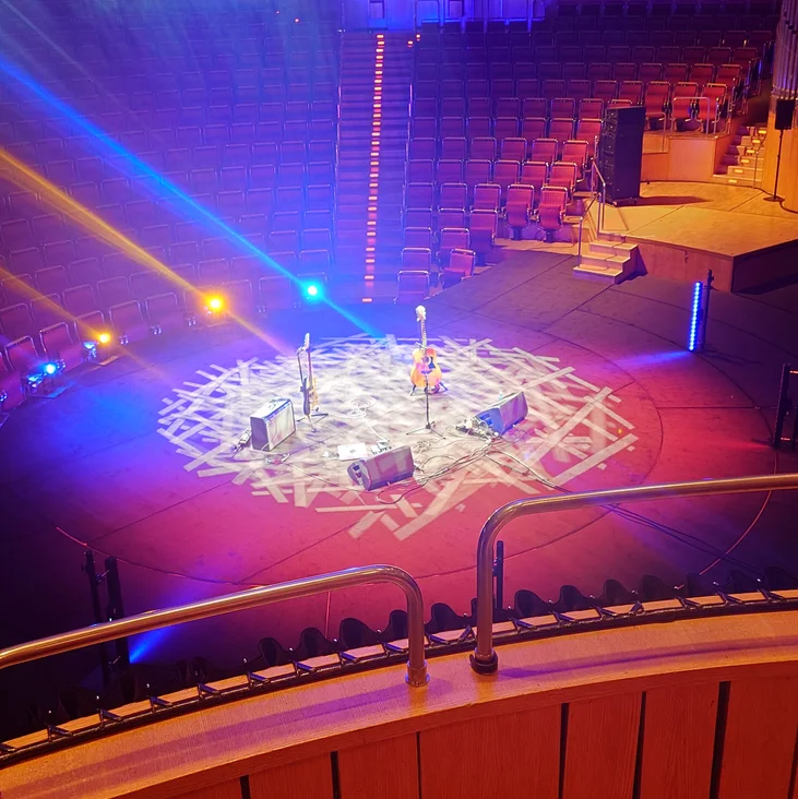 Ein leerer runder Bühnenbereich mit bunten Lichtern und einem dekorativen Muster. Sitzplätze sind im Hintergrund sichtbar.