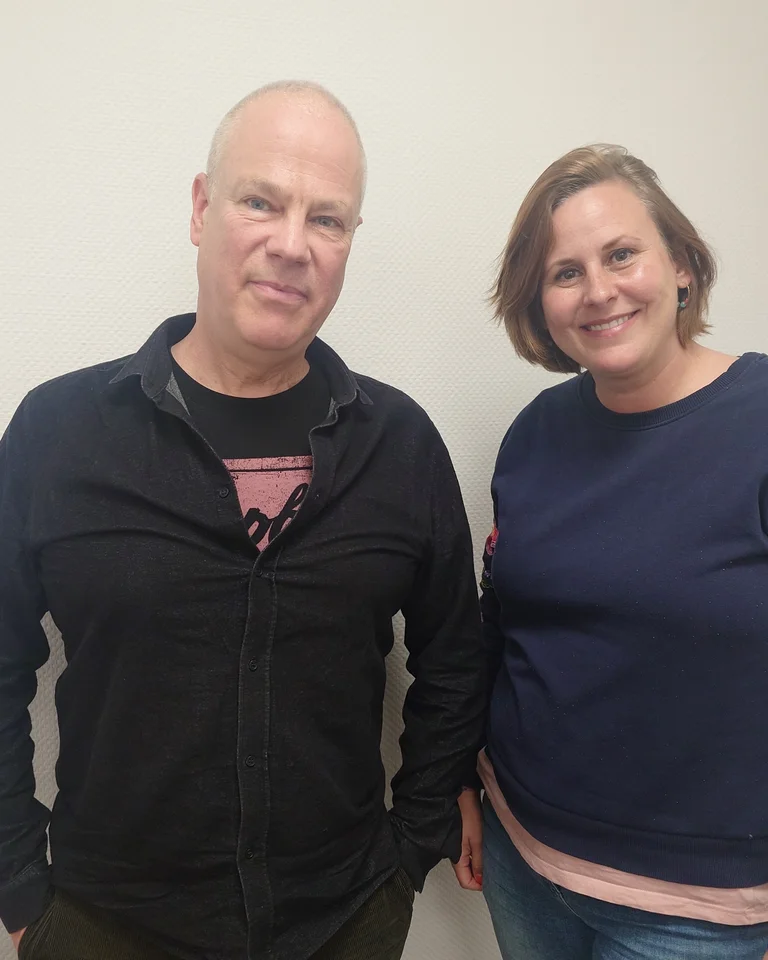 Zwei Personen (Prof. Dr. Anno Mungen und Katie Knees) stehen lächelnd nebeneinander vor einem weißen Hintergrund. Beide tragen lässige Kleidung.