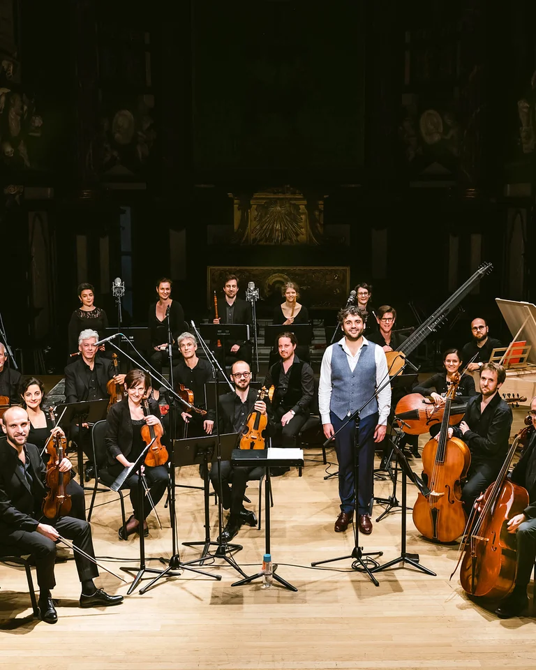 Ein Kammerorchester auf einer Bühne mit ihren Instrumenten. Die Musiker sind formell gekleidet und bereit für eine Aufführung.