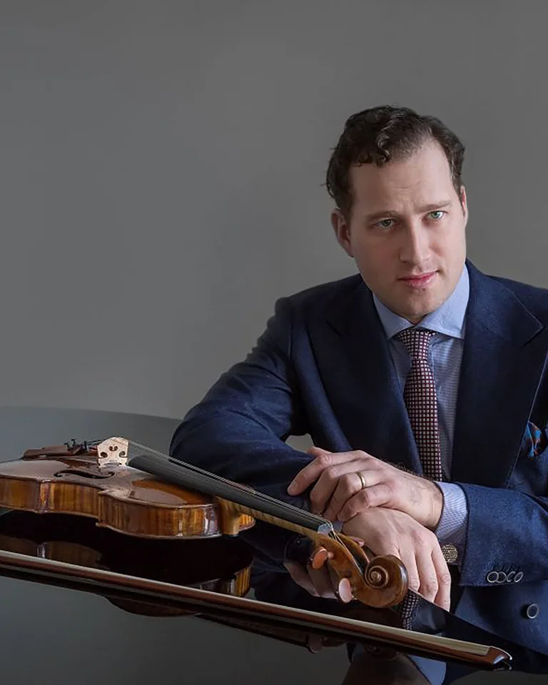 Ein Mann in einem dunkelblauen Anzug lehnt sich auf einen Tisch mit einer Geige und einem Bogen.