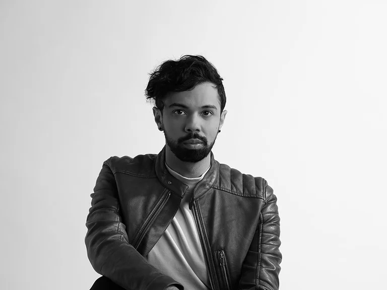 Schwarz-weiß Foto eines Mannes (Bruno de Sá) in Lederjacke, der auf einer Kiste hockt. Der Hintergrund ist schlicht und hell.