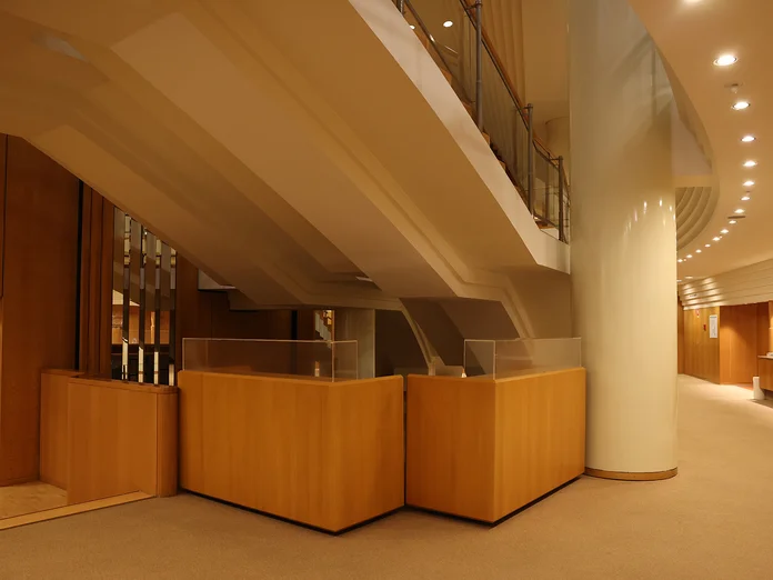 Bar im unteren Foyer der Kölner Philharmonie: Ein modernes Foyer mit geschwungenen Treppen, Holzakzenten und moderner Beleuchtung, das auf eine elegante architektonische Gestaltung hinweist.