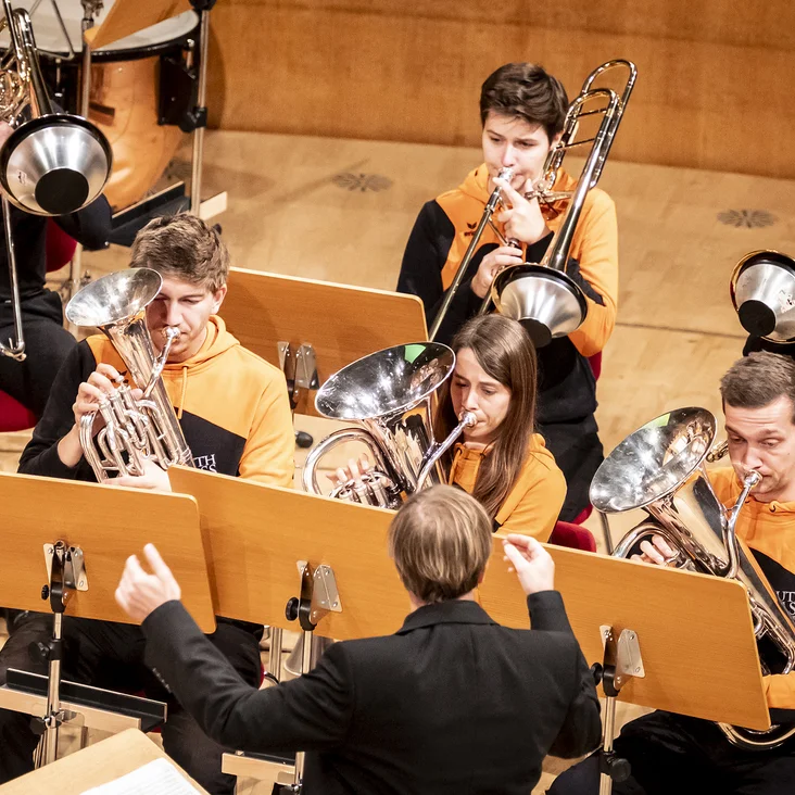 Martin Schädlich with Youth Brass Band NRW e.V. : A youth orchestra playing brass instruments on stage. The conductor leads them as they perform with focus.