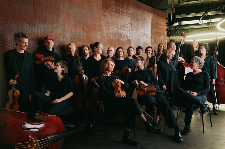 The members of Ensemble Resonanz pose dressed in black and have instruments such as violins and double basses with them.
