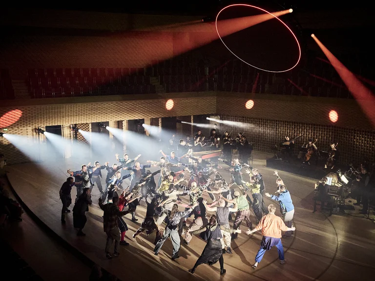 Group dance (Structure Rualitè mit Capella Mediterranea u.a.) performance on stage with dramatic lighting. Dancers are in colorful costumes, spotlight focused on them.