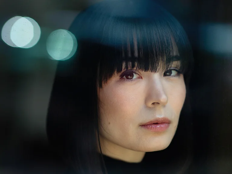 Porträt einer Frau (Alice Sara Ott) mit dunklem, glattem Haar und Pony, die nachdenklich in die Kamera blickt.