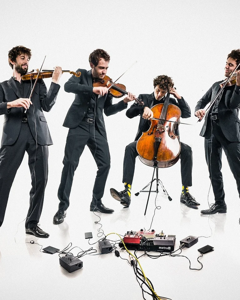 Vier Musiker in Anzügen (vision string quartet) spielen Streichinstrumente in einem modernen Setting. Kabel und Pedale liegen auf dem Boden.