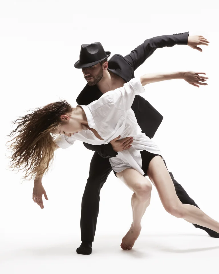 Ein Paar tanzt eindrucksvoll, mit einem Mann im Anzug und einer Frau im weißen Hemd. Sie posieren dynamisch.