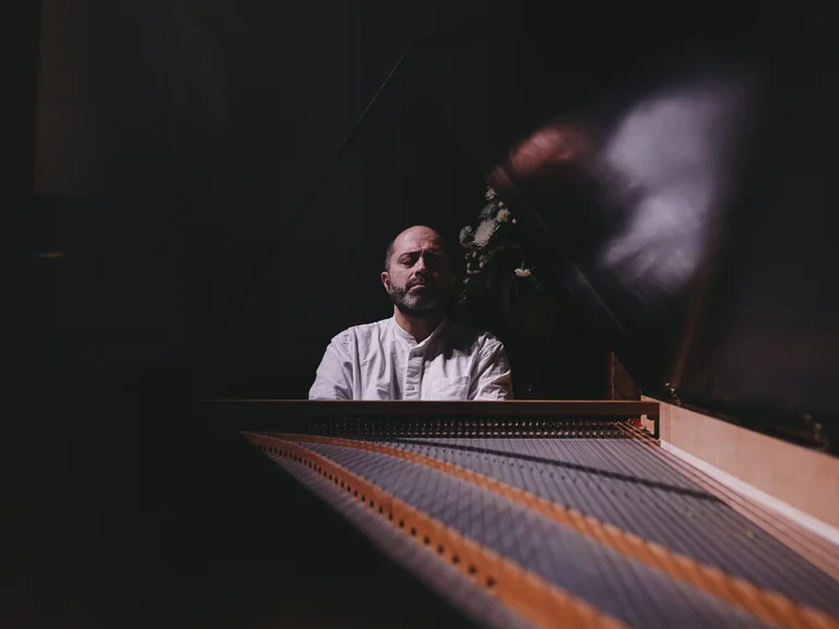 Ein Mann (Mahan Esfahani)sitzt am Cembalo, im Hintergrund dunkle Beleuchtung. Der Fokus liegt auf den Saiten und der Tastatur.